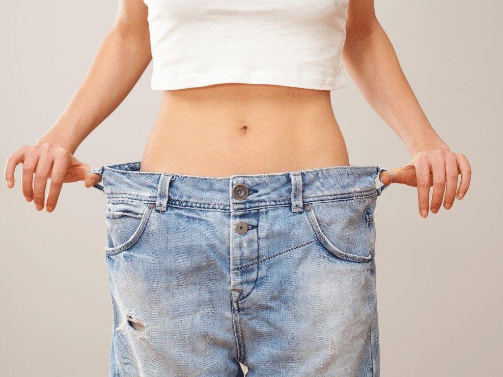 Person wearing loose jeans after weight loss, and the benefits of intermittent fasting and calorie restriction.