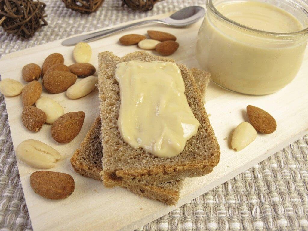 Whole grain bread topped with almond butter and surrounded by nuts, a quick meal prep snack for busy mornings.