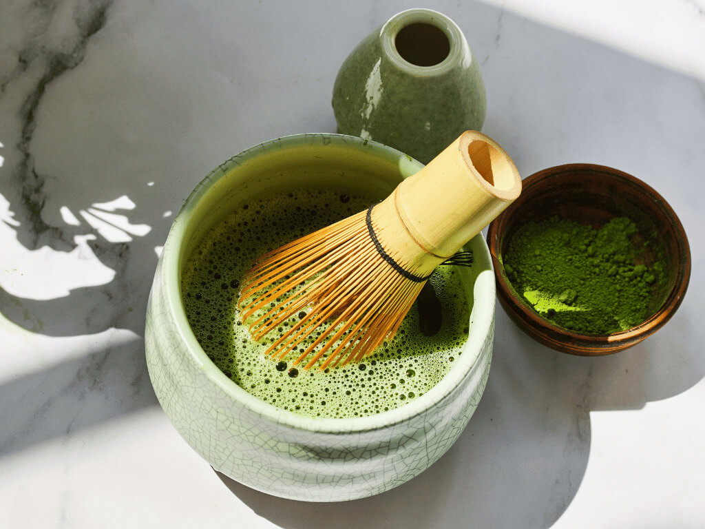 bowl of matcha with bamboo whisk and matcha powder in a smaller bowl representing best matcha powder