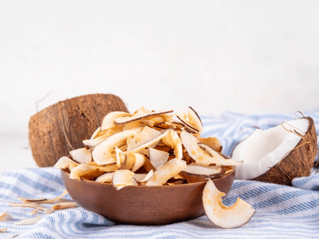 Bowl of unsweetened coconut chips on a table, a crunchy gluten-free snack rich in healthy fats and natural sweetness.