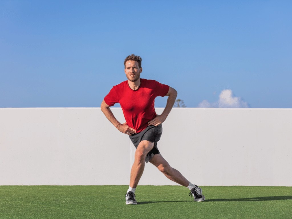 A man doing curtsy lunges outdoors on grass, engaging lower body muscle groups and burning thigh fat through strength training.
