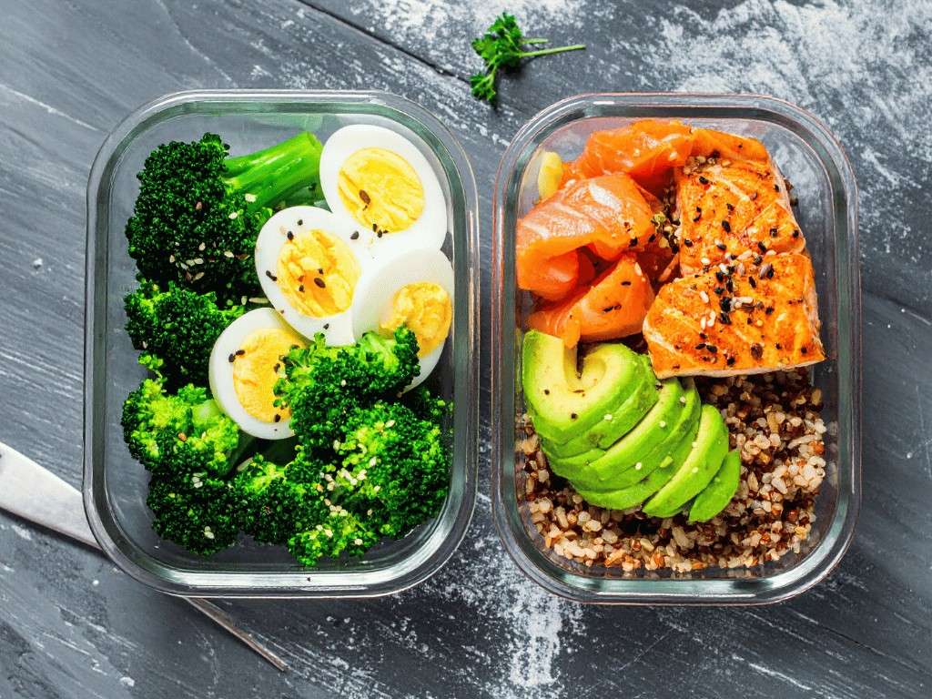Meal prep containers with salmon, avocado, eggs, and broccoli, balanced meals for intermittent fasting and weight loss.