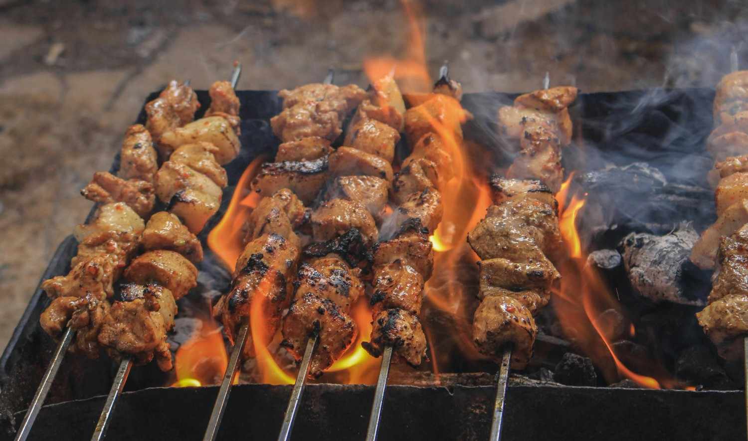 Grilled meat skewers cooking over open flame, a high fat and low carb meal suitable for keto and paleo diets.