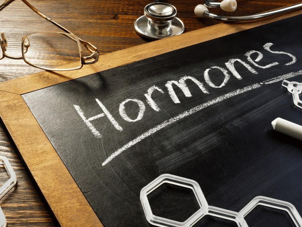 Chalkboard labeled hormones with medical tools symbolizing hormonal imbalance linked to unexplained weight gain.