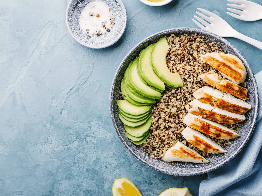 Low FODMAP grilled lemon herb chicken with quinoa and avocado slices in a bowl.