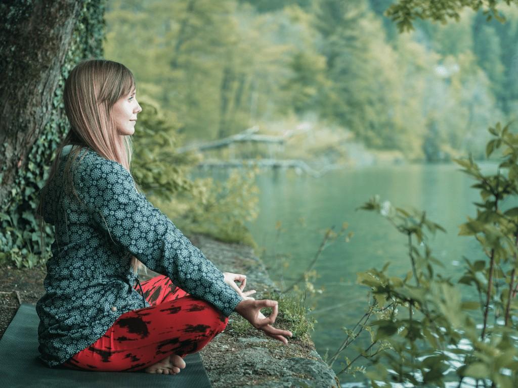 Woman meditating outdoors near a lake to lower cortisol levels through mindfulness and stress reduction