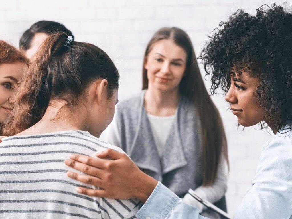 Support group comforting young woman during eating disorder recovery discussion.