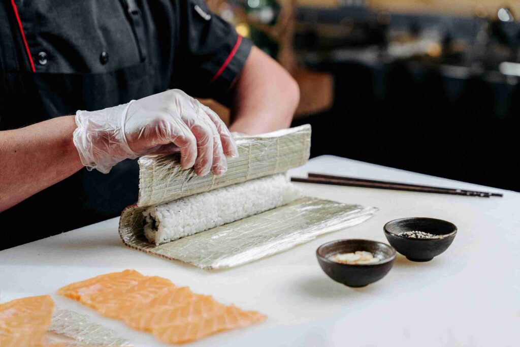 Chef preparing sushi roll with rice and seaweed on a bamboo mat, showing is sushi healthy ingredients like fish, rice, and balanced seasonings.