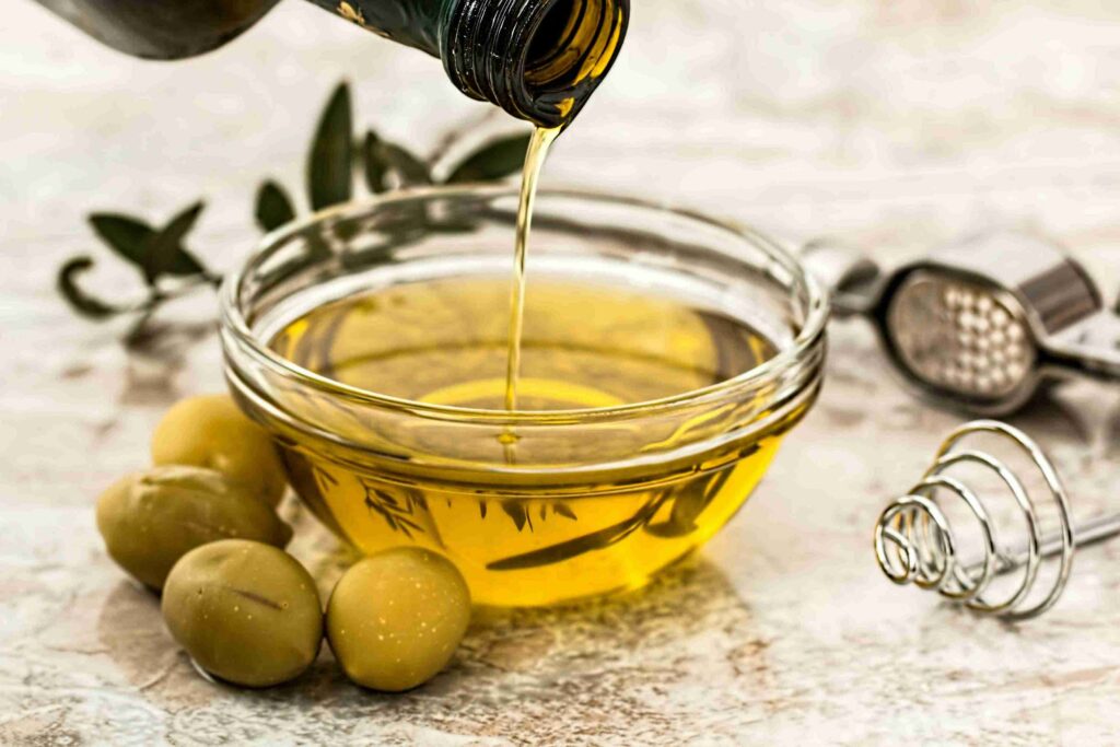 olive oil being poured into a glass bowl beside fresh olives, a staple healthy fat in paleo food list that supports heart health.