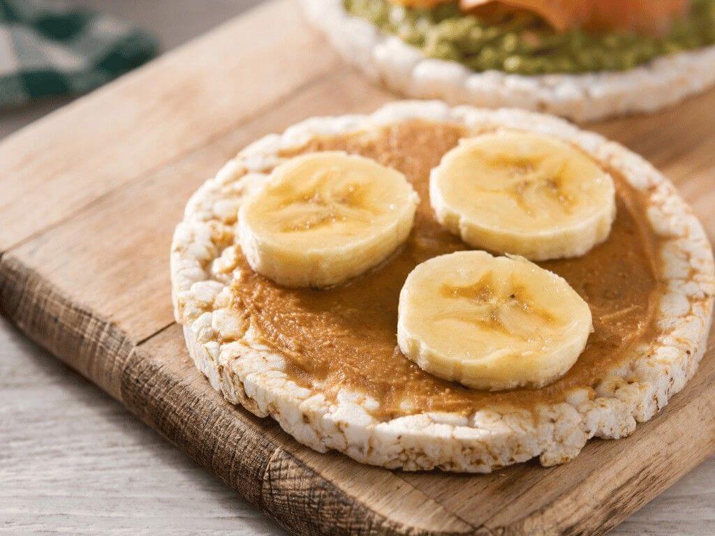 Crunchy rice cake topped with creamy almond butter and banana slices, a healthy snack rich in carbs and protein.