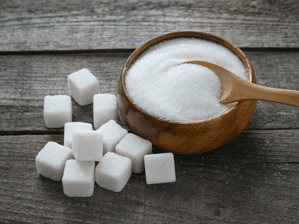 Wooden bowl of granulated sugar and sugar cubes with a wooden spoon.