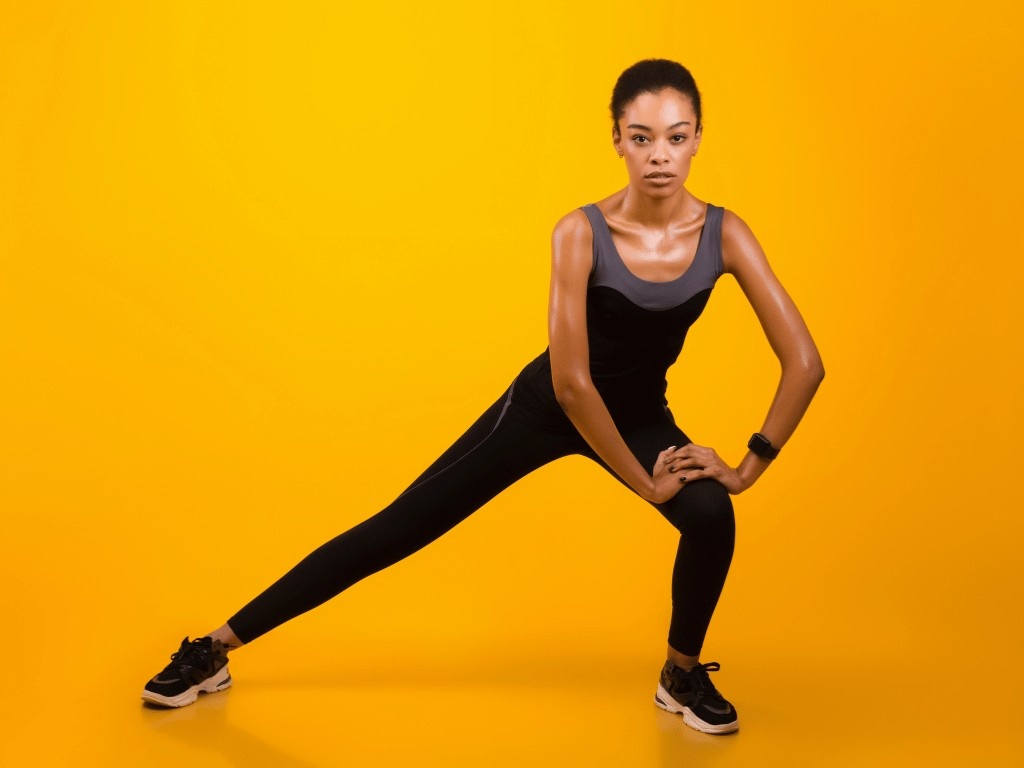 A woman performing a side lunge stretch in fitness wear, targeting inner thigh muscles and promoting lower body fat loss with Eato.