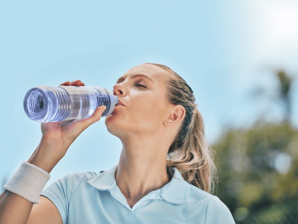 Woman drinking water outdoors after a workout, maintaining hydration and supporting metabolic health during fasting.
