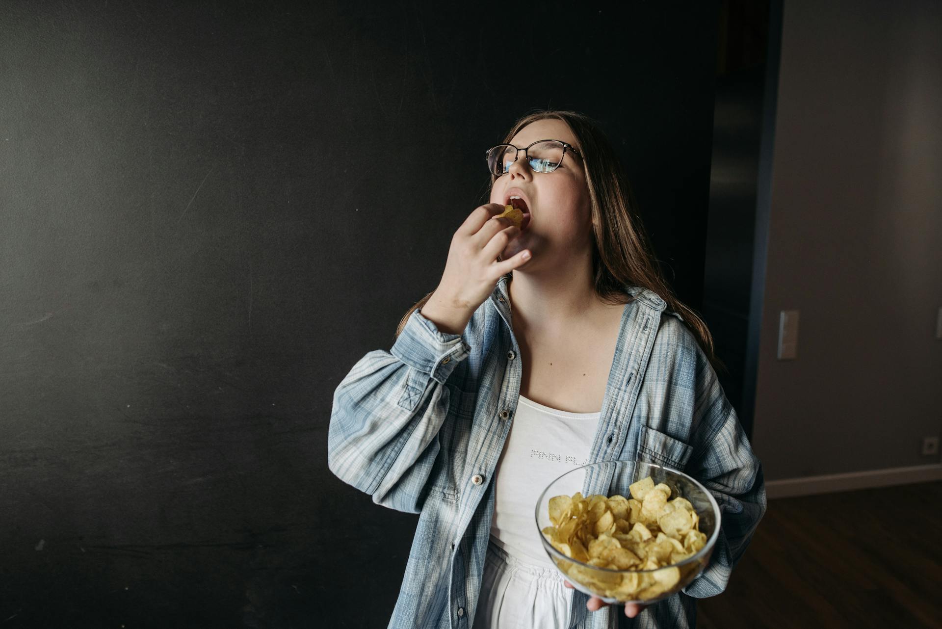 Woman eating potato chips from a bowl, stress eating behavior linked to emotional comfort.