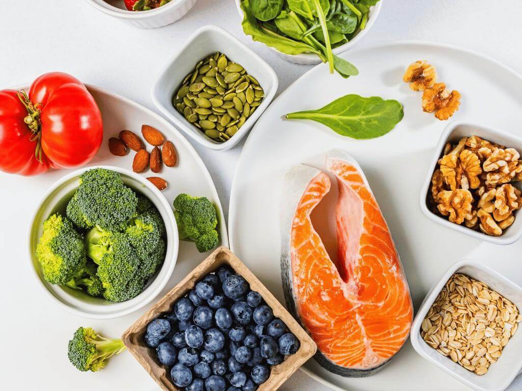 Paleo food list include salmon, nuts, spinach, and broccoli on a white plate.
