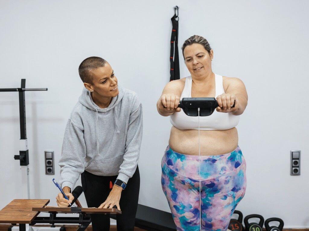 Fitness trainer measuring woman’s body composition using handheld device to assess body fat and muscle mass.
