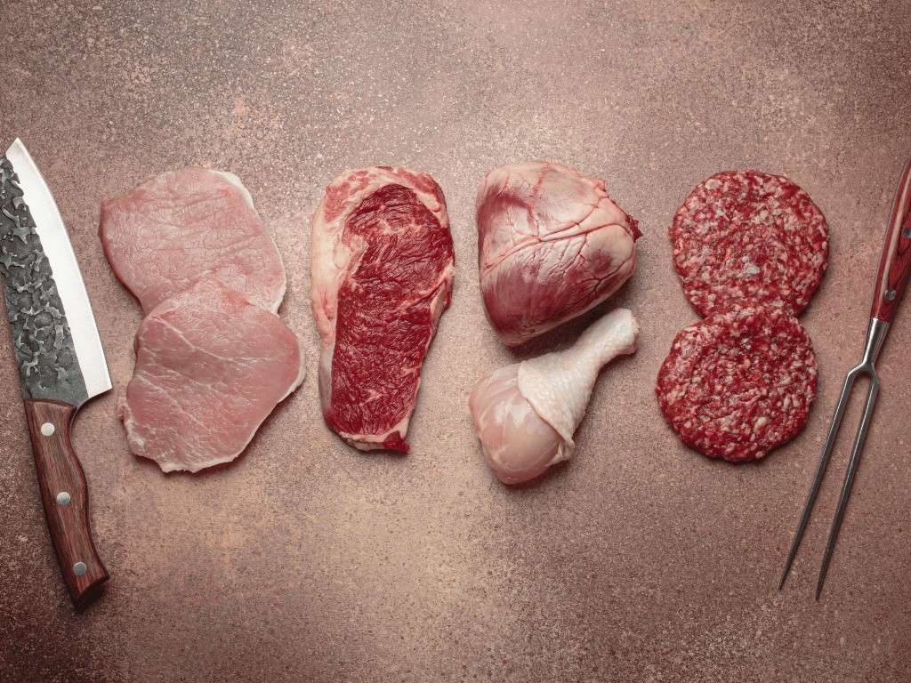 Raw beef, chicken, and steak cuts arranged beside knife for carnivore diet.