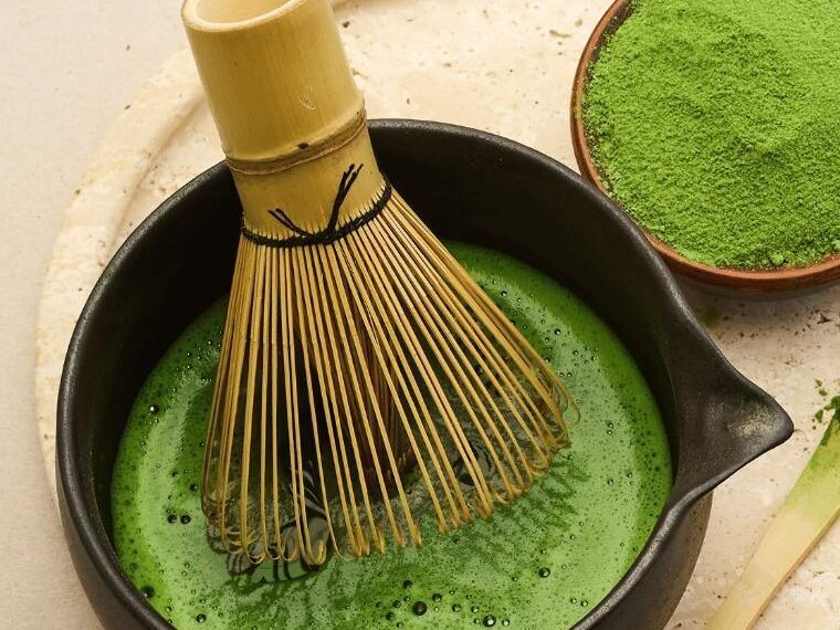 Bowl of vibrant green matcha tea with bamboo whisk and powdered tea a traditional Japanese preparation.