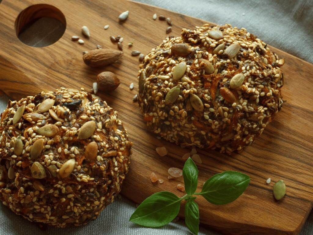 Two paleo bread rolls topped with nuts and seeds on wooden board