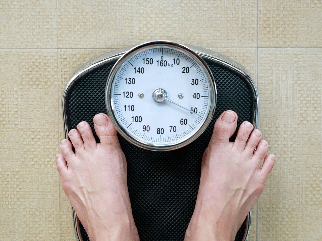 Person standing on scale showing sudden unexplained weight gain without changes in diet or activity.