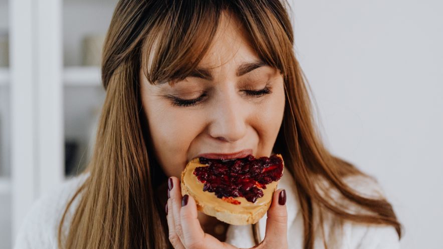 A woman is biting into a piece of jam-covered bread.