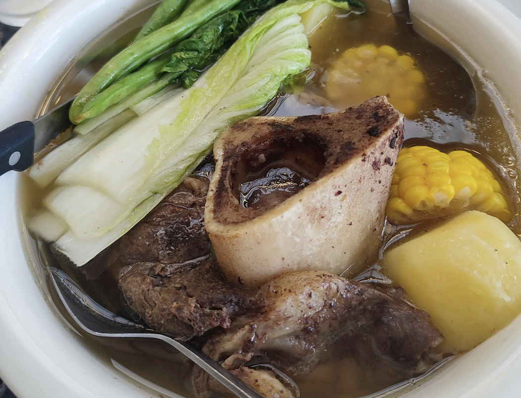 Beef bone broth with marrow bone, leafy greens, corn, and potatoes simmered in a clear, nutrient rich broth