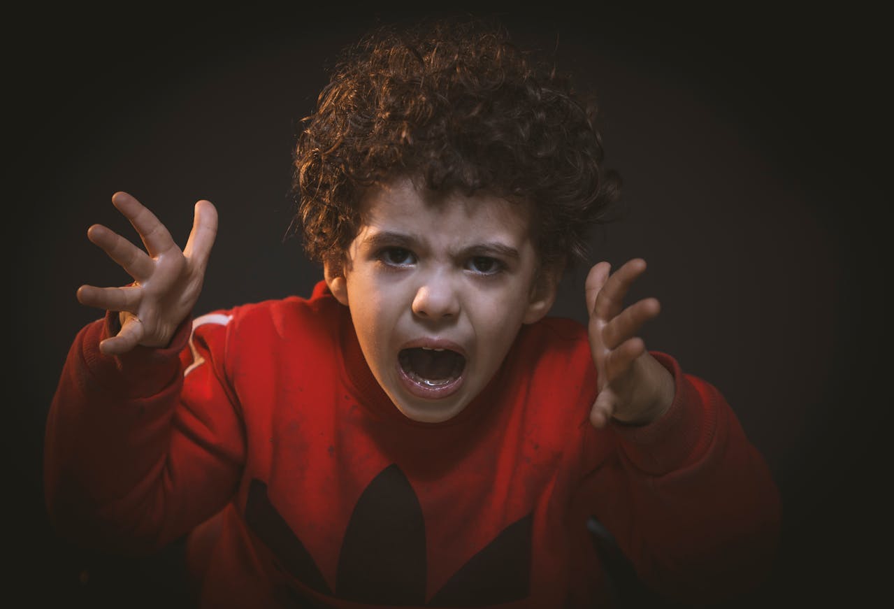 Child wearing a red sweater shouting with hands raised, showing anger and frustration, likely because he is hangry.