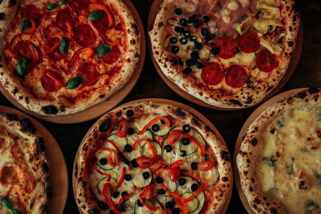 High carbohydrate foods can contribute to bloating. Five sourdough pizzas with toppings arranged together on a table.
