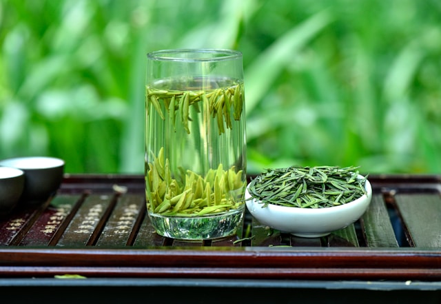 Green tea leaves steeping in a clear glass beside fresh leaves on a tray. Does green tea help with weight loss?
