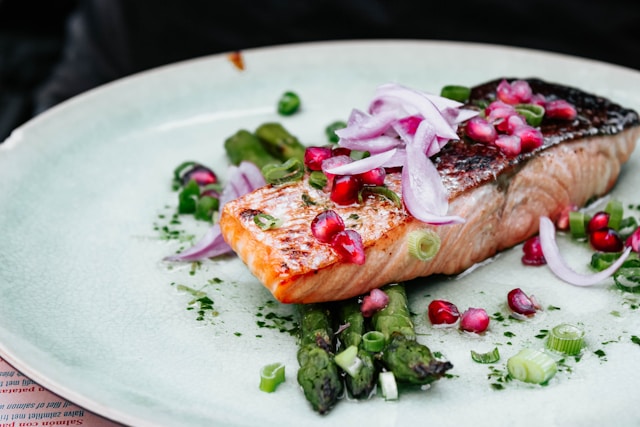 Grilled salmon with pomegranate seeds, sliced onions, and asparagus served as a low carb meal suitable for the
Modified Atkins Diet.