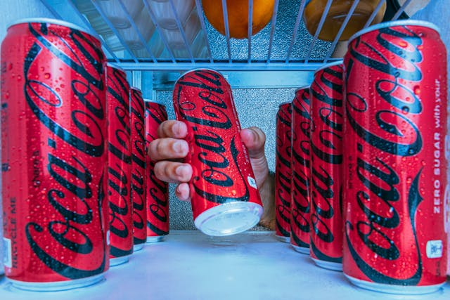 Multiple Coke Zero cans inside a refrigerator with a hand reaching in.