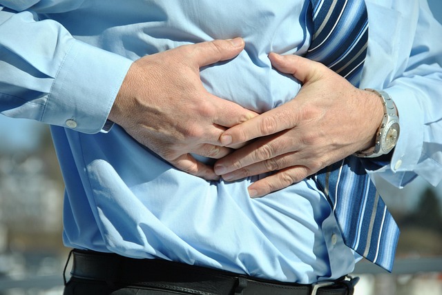 Man in a blue shirt holding his abdomen with both hands while his stomach appears tight and uncomfortable, due to bloating after eating.