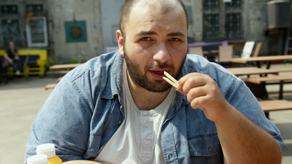 Man eating fries and drinking a sugary beverage wirh sedentary habits that can cause Lexapro weight gain risk