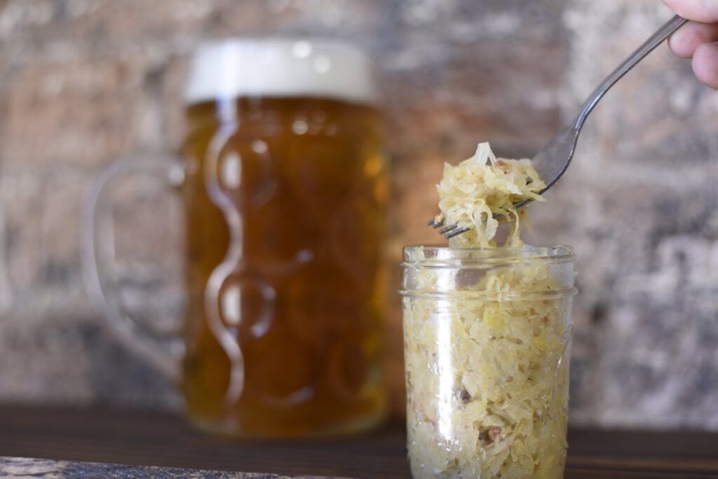 Fork lifting sauerkraut from a jar with a beer mug in the background, fermented food for gut microbiota support