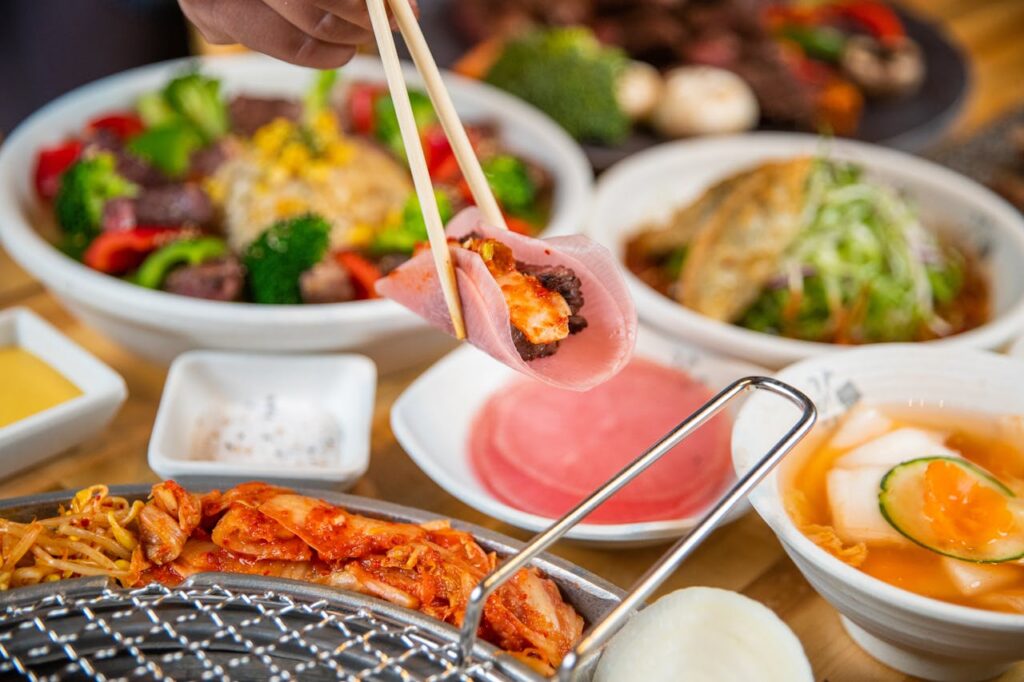 Chopsticks lifting kimchi over Korean side dishes on a shared table, a fermented food spread.