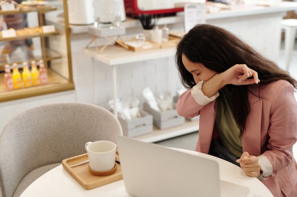 Woman sneezing at a café table while using a laptop
