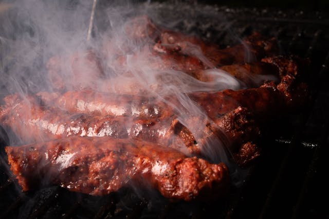 Grilled dried ossban sausages smoking over charcoal, showing Tunisian fermented meat with a dark spiced crust.