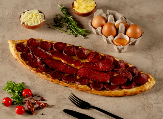 Turkish sucuk slices baked on flatbread with eggs, herbs, cheese, and tomatoes.