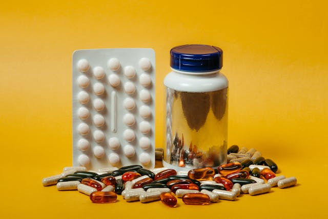 Vitamins and supplements scattered beside a bottle on a yellow background.