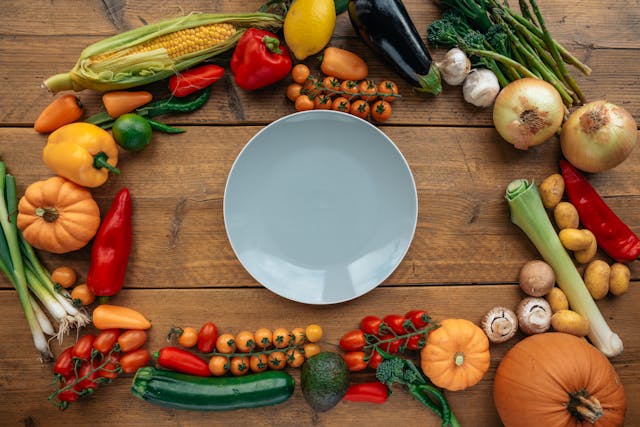 An empty plate surrounded by vegetables on a wooden table, intermittent fasting eating window.