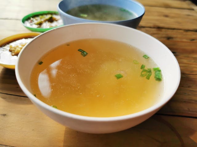 Bowl of clear bone broth with scallions on a wooden table. Does bone broth break a fast?